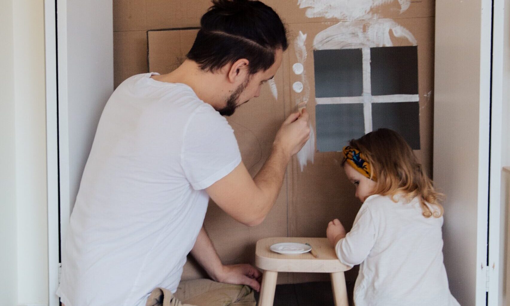 A man and a little girl painting a cardboard playhouse